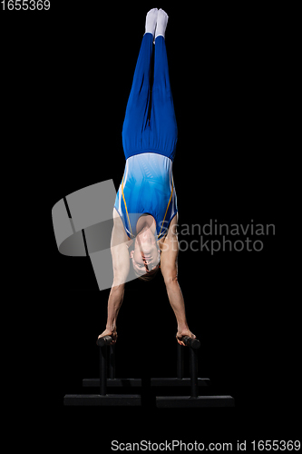 Image of Muscular male gymnast training in gym, flexible and active. Caucasian fit guy, athlete in blue sportswear isolated on black