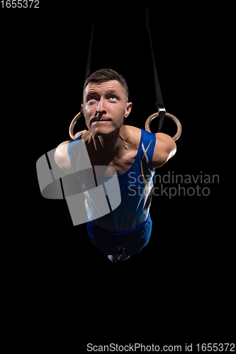 Image of Muscular male gymnast training in gym, flexible and active. Caucasian fit guy, athlete in blue sportswear isolated on black