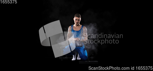 Image of Muscular male gymnast training in gym, flexible and active. Caucasian fit guy, athlete in blue sportswear isolated on black