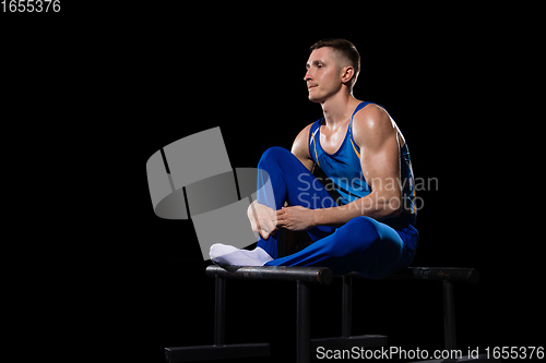 Image of Muscular male gymnast training in gym, flexible and active. Caucasian fit guy, athlete in blue sportswear isolated on black