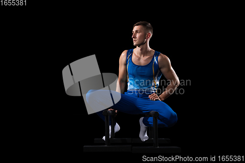 Image of Muscular male gymnast training in gym, flexible and active. Caucasian fit guy, athlete in blue sportswear isolated on black