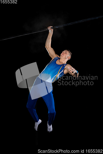 Image of Muscular male gymnast training in gym, flexible and active. Caucasian fit guy, athlete in blue sportswear isolated on black