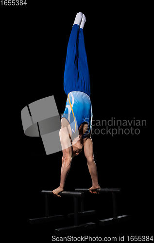 Image of Muscular male gymnast training in gym, flexible and active. Caucasian fit guy, athlete in blue sportswear isolated on black