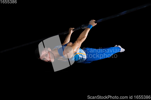 Image of Muscular male gymnast training in gym, flexible and active. Caucasian fit guy, athlete in blue sportswear isolated on black