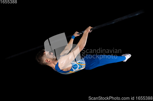 Image of Muscular male gymnast training in gym, flexible and active. Caucasian fit guy, athlete in blue sportswear isolated on black