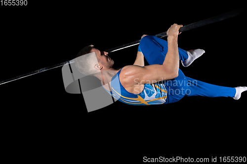 Image of Muscular male gymnast training in gym, flexible and active. Caucasian fit guy, athlete in blue sportswear isolated on black