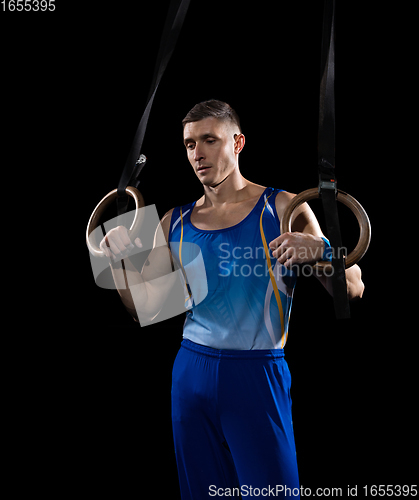 Image of Muscular male gymnast training in gym, flexible and active. Caucasian fit guy, athlete in blue sportswear isolated on black