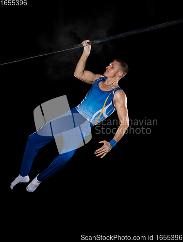 Image of Muscular male gymnast training in gym, flexible and active. Caucasian fit guy, athlete in blue sportswear isolated on black