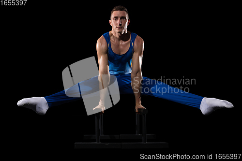 Image of Muscular male gymnast training in gym, flexible and active. Caucasian fit guy, athlete in blue sportswear isolated on black