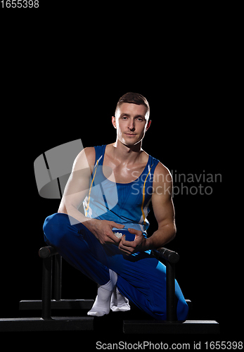 Image of Muscular male gymnast training in gym, flexible and active. Caucasian fit guy, athlete in blue sportswear isolated on black