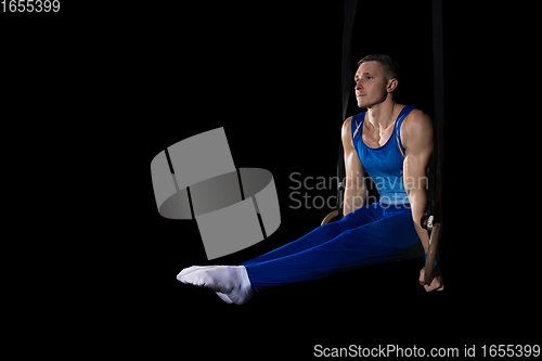 Image of Muscular male gymnast training in gym, flexible and active. Caucasian fit guy, athlete in blue sportswear isolated on black