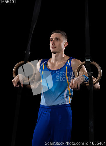 Image of Muscular male gymnast training in gym, flexible and active. Caucasian fit guy, athlete in blue sportswear isolated on black