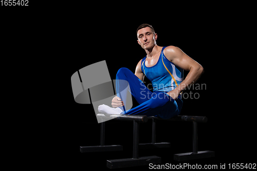 Image of Muscular male gymnast training in gym, flexible and active. Caucasian fit guy, athlete in blue sportswear isolated on black