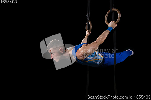 Image of Muscular male gymnast training in gym, flexible and active. Caucasian fit guy, athlete in blue sportswear isolated on black