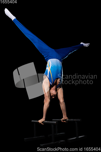 Image of Muscular male gymnast training in gym, flexible and active. Caucasian fit guy, athlete in blue sportswear isolated on black