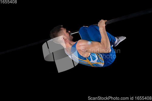 Image of Muscular male gymnast training in gym, flexible and active. Caucasian fit guy, athlete in blue sportswear isolated on black