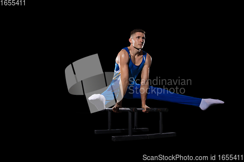 Image of Muscular male gymnast training in gym, flexible and active. Caucasian fit guy, athlete in blue sportswear isolated on black