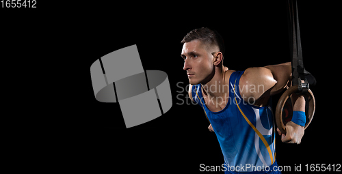 Image of Muscular male gymnast training in gym, flexible and active. Caucasian fit guy, athlete in blue sportswear isolated on black