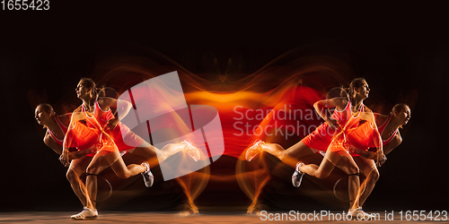 Image of Young woman playing tennis isolated on black with fire flames. Youth, flexibility, power and energy. Reflection, mirror, strobe light