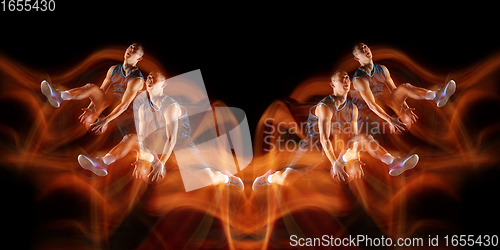 Image of Young purposeful basketball player training in action isolated on black background with fire flames. Mirror, strobe light effect, reflection