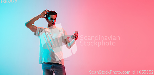 Image of Young caucasian man\'s portrait on gradient blue-pink studio background in neon light