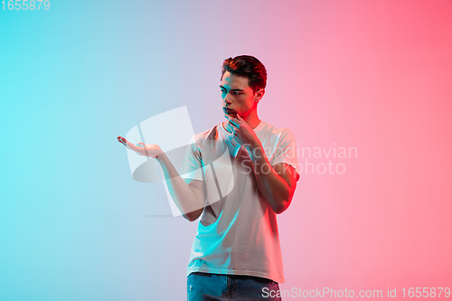 Image of Young caucasian man\'s portrait on gradient blue-pink studio background in neon light