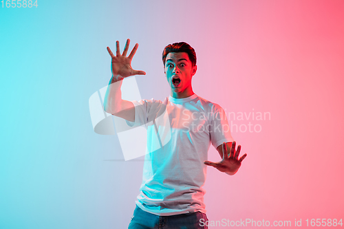 Image of Young caucasian man\'s portrait on gradient blue-pink studio background in neon light