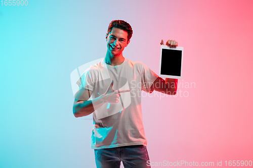 Image of Young caucasian man\'s portrait on gradient blue-pink studio background in neon light