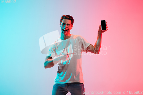 Image of Young caucasian man\'s portrait on gradient blue-pink studio background in neon light