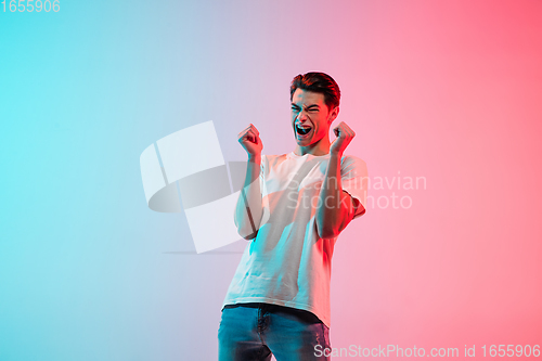 Image of Young caucasian man\'s portrait on gradient blue-pink studio background in neon light