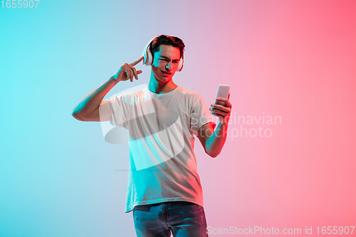 Image of Young caucasian man\'s portrait on gradient blue-pink studio background in neon light