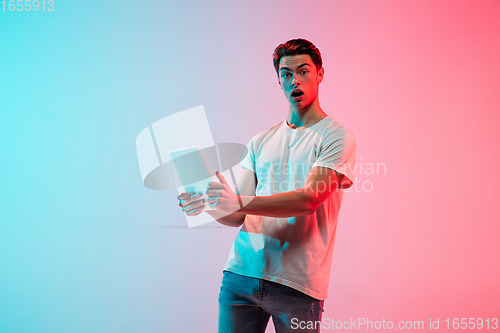 Image of Young caucasian man\'s portrait on gradient blue-pink studio background in neon light