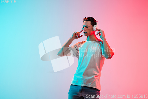 Image of Young caucasian man\'s portrait on gradient blue-pink studio background in neon light