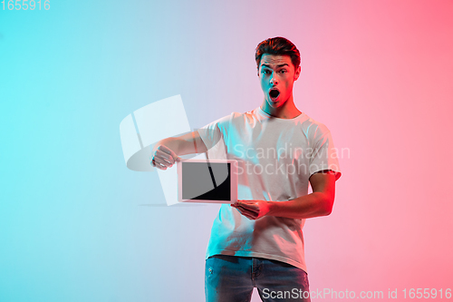 Image of Young caucasian man\'s portrait on gradient blue-pink studio background in neon light