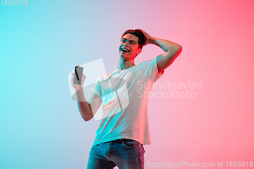 Image of Young caucasian man\'s portrait on gradient blue-pink studio background in neon light