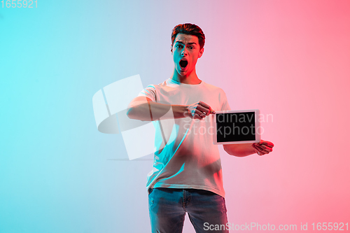 Image of Young caucasian man\'s portrait on gradient blue-pink studio background in neon light