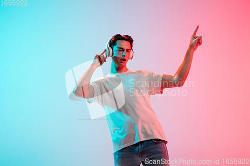 Image of Young caucasian man\'s portrait on gradient blue-pink studio background in neon light