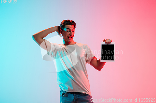 Image of Young caucasian man\'s portrait on gradient blue-pink studio background in neon light