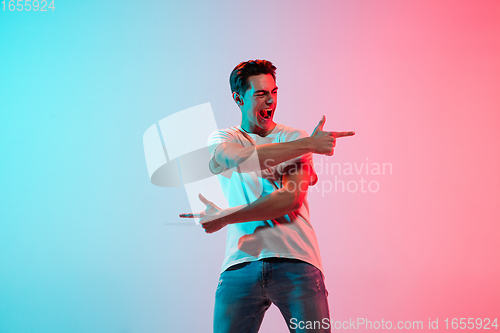 Image of Young caucasian man\'s portrait on gradient blue-pink studio background in neon light