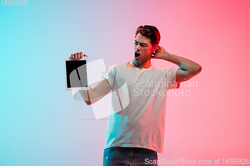Image of Young caucasian man\'s portrait on gradient blue-pink studio background in neon light