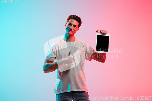 Image of Young caucasian man\'s portrait on gradient blue-pink studio background in neon light