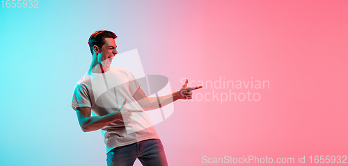 Image of Young caucasian man\'s portrait on gradient blue-pink studio background in neon light