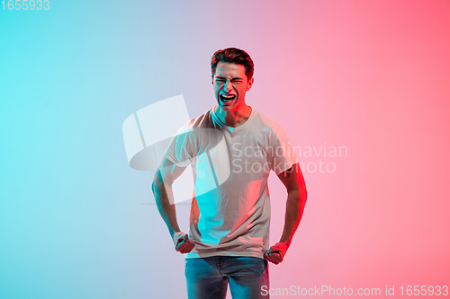 Image of Young caucasian man\'s portrait on gradient blue-pink studio background in neon light