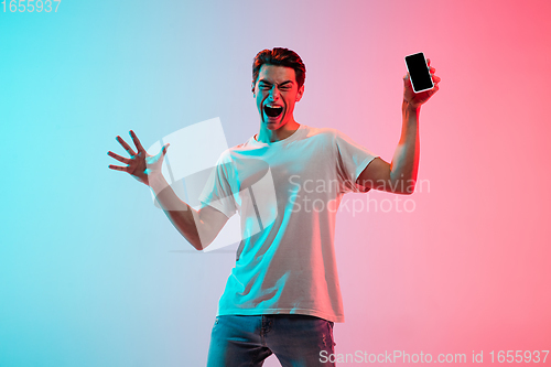 Image of Young caucasian man\'s portrait on gradient blue-pink studio background in neon light