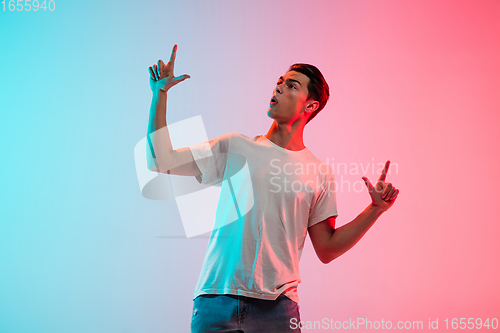 Image of Young caucasian man\'s portrait on gradient blue-pink studio background in neon light