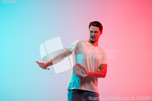 Image of Young caucasian man\'s portrait on gradient blue-pink studio background in neon light