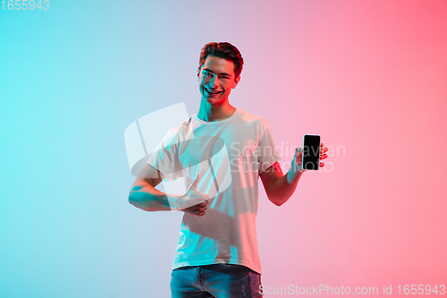 Image of Young caucasian man\'s portrait on gradient blue-pink studio background in neon light