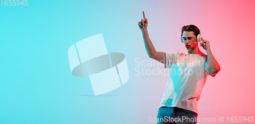 Image of Young caucasian man\'s portrait on gradient blue-pink studio background in neon light