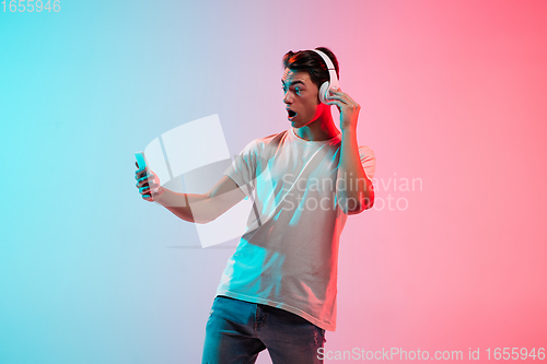Image of Young caucasian man\'s portrait on gradient blue-pink studio background in neon light