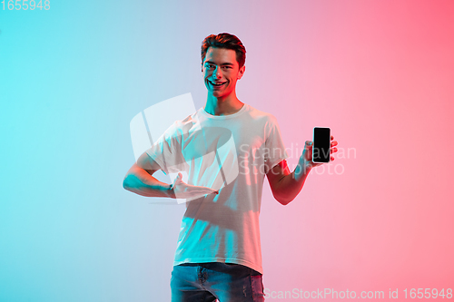 Image of Young caucasian man\'s portrait on gradient blue-pink studio background in neon light